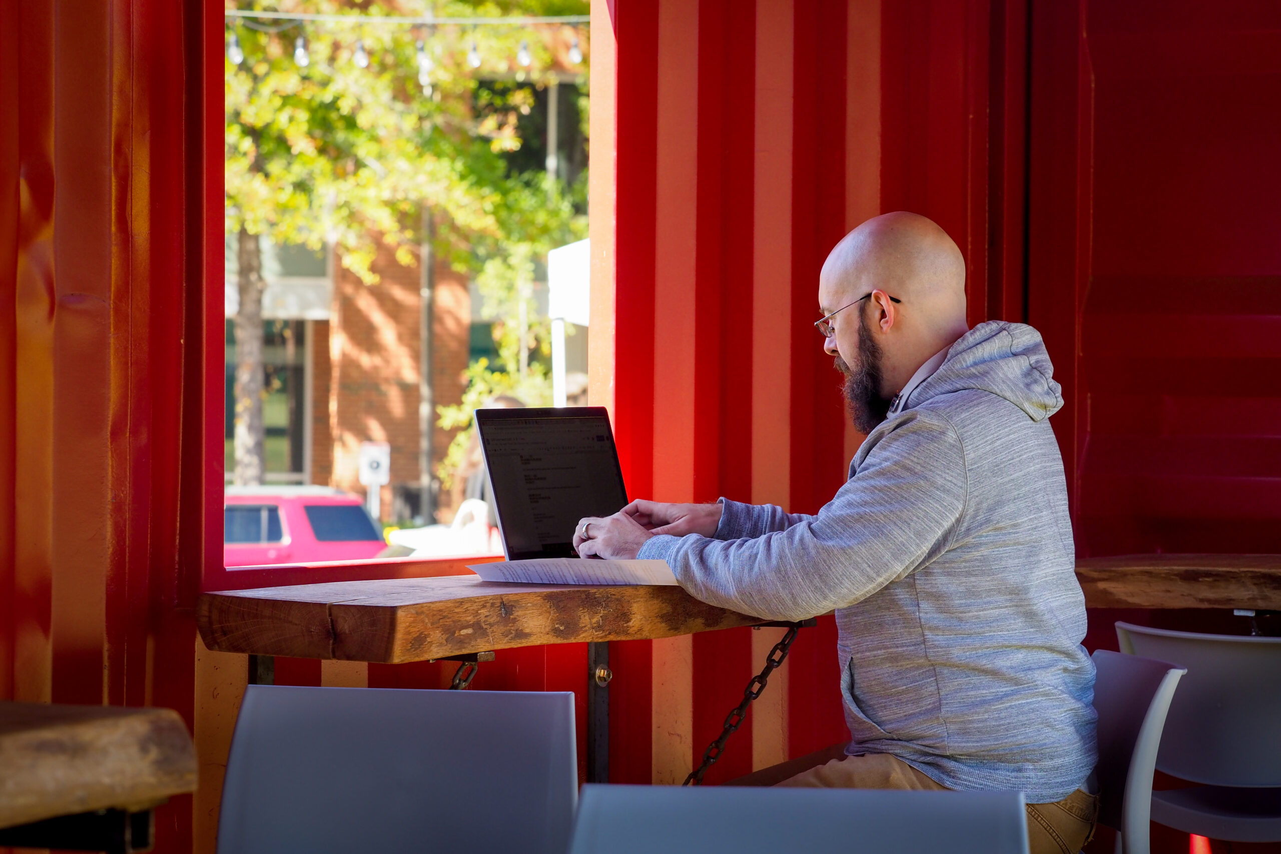 A student sitting in a shaded part of NCSU Centennial Campus typing on the open laptop in front of him. 