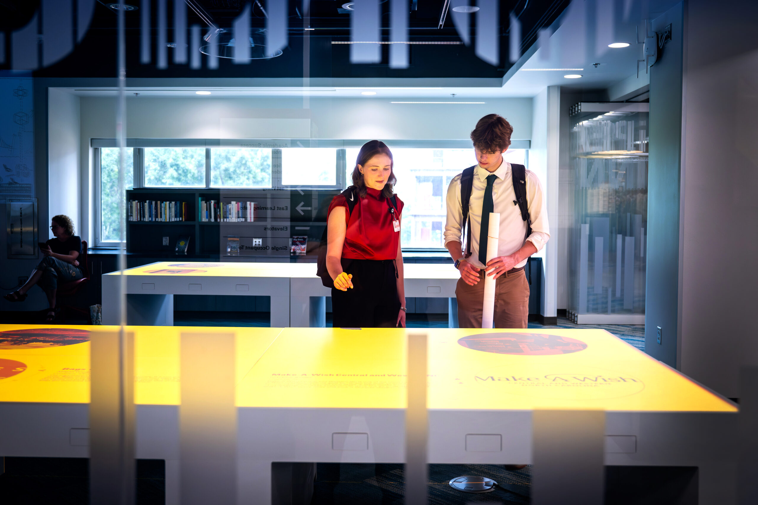 Two individuals observe a brightly lit digital exhibit projected on a table at the iPearl Innovation Studio in Hunt Library. 